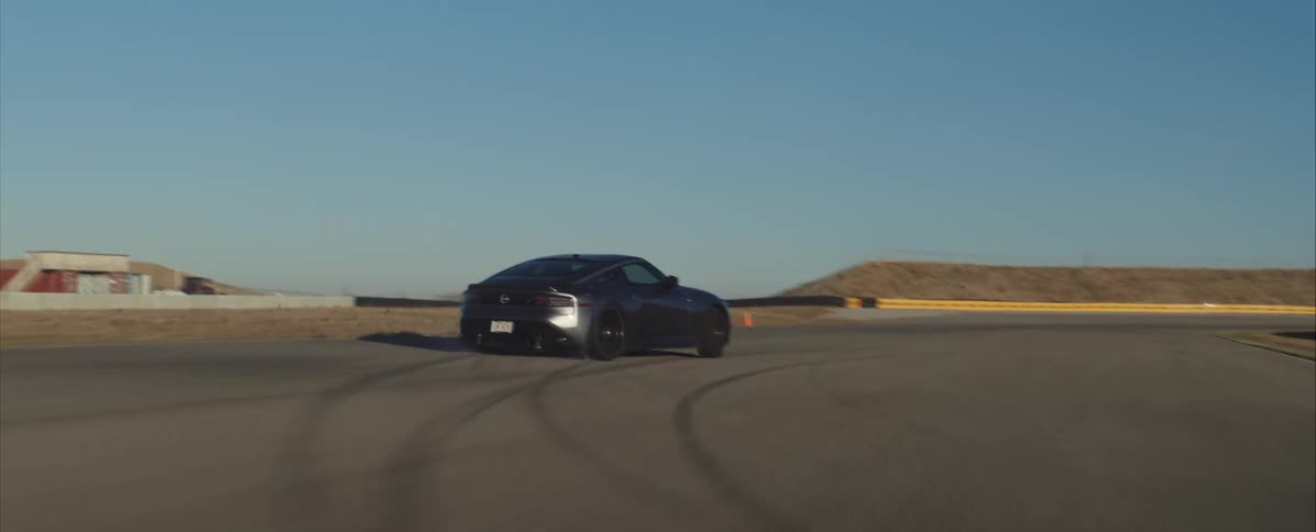 Dark sports car drifting on track curve with orange cone and visible tire marks