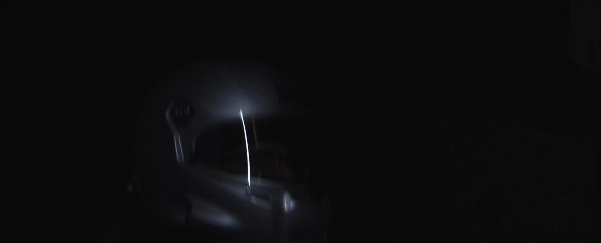 A helmet in a black void catching a bright light reflection on its dark visor