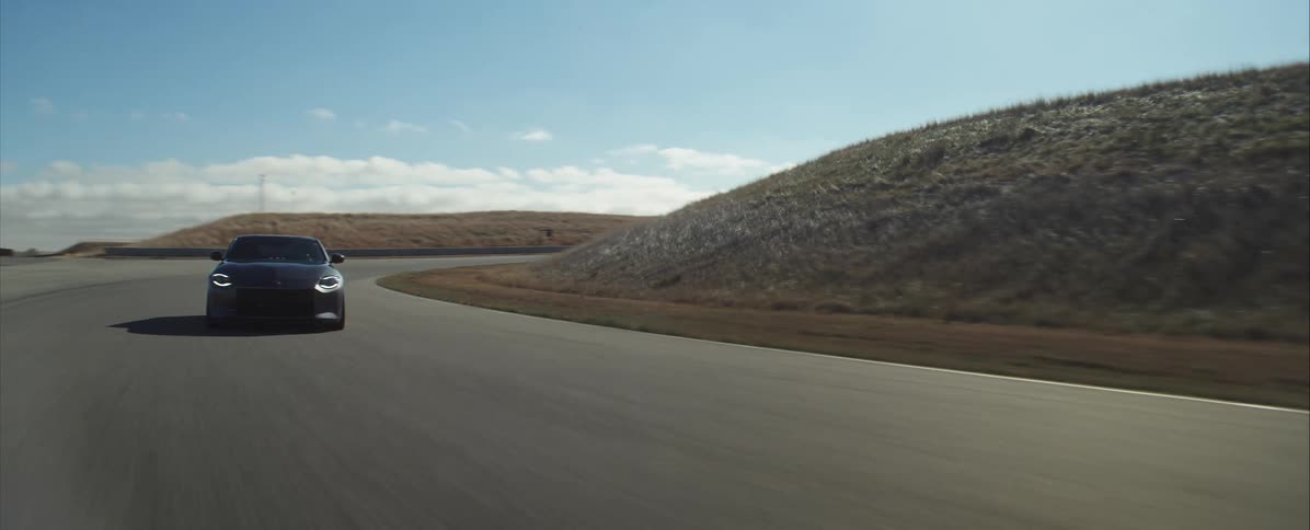 A dark sports car speeds along a sunlit asphalt racetrack maneuvering a corner with dry hills and a bright blue sky framing its highperformance drive