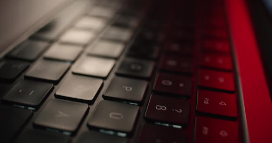 A computer keyboard glows with red light illuminating the dark room around it