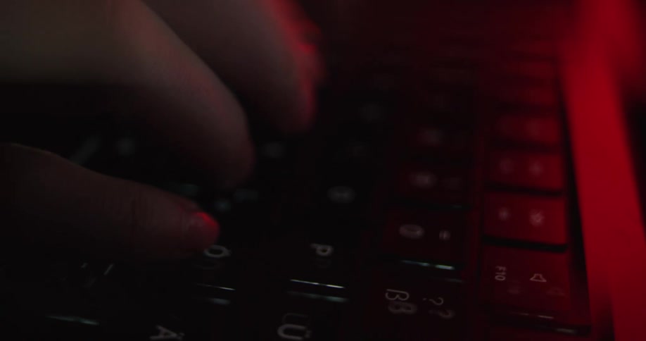 Fingers typing on keyboard lit by red light
