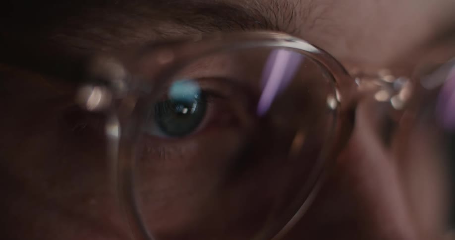 The computer screen reflects on the mans glasses