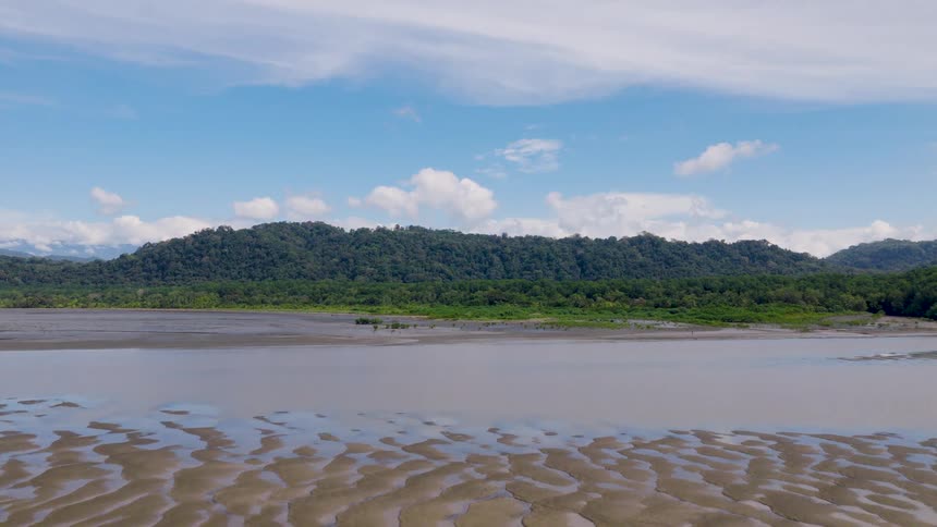 Peaceful beach with wet sand shallow water reflecting sky and lush hill in the background