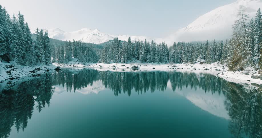 I see a still beautiful scene which can be described in two linesa tranquil lake perfectly mirrors a dense forest of snowdusted pine treesthe backdrop is composed of majestic snowcovered mountains under a bright clear sky