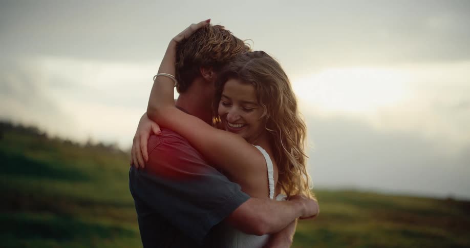 A happy couple hugging each other while standing outdoors in a grass field during daytime