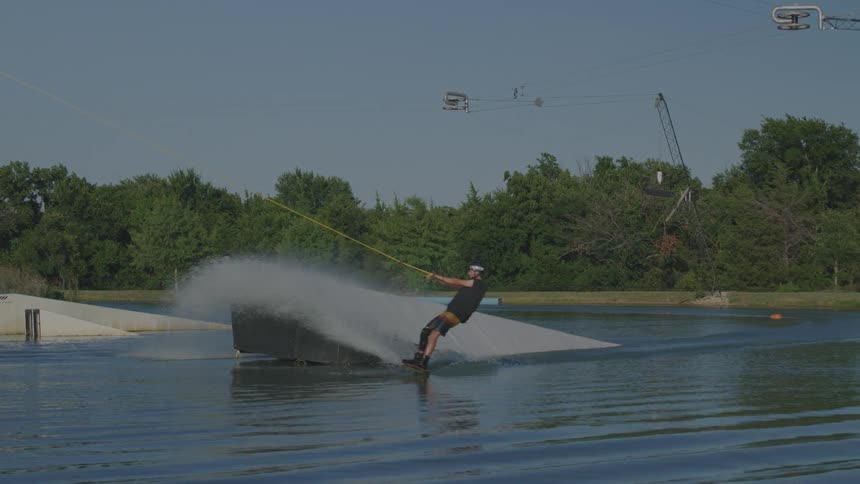 A young man is wingboarding on a river at midday wearing a helmet