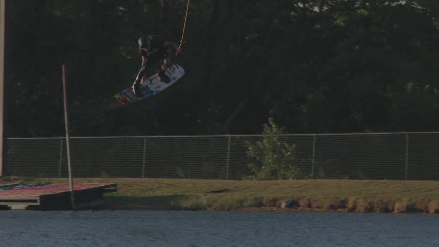 A wakeboarder jumps off a ramp over the water while being pulled by a cable