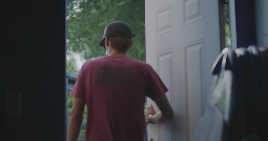 A man walks in a room past several surfboard propped up against a wall as he walks outside