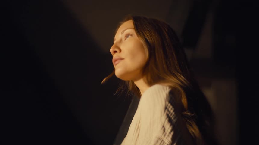 Woman lit by warm light looking upward in an indoor setting