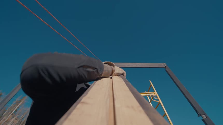 A carpenter climbing a ladder up toward the roof during an outdoor construction project at midday