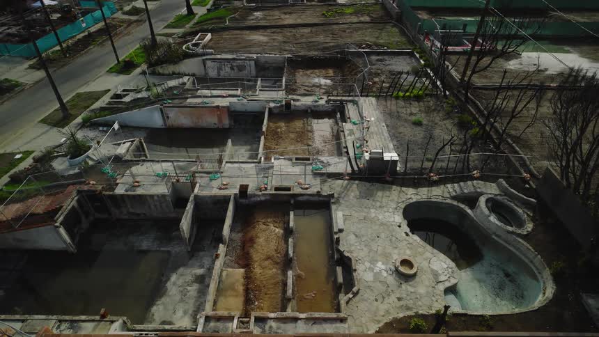 Ruins of a residential structure with exposed foundations and an empty pool