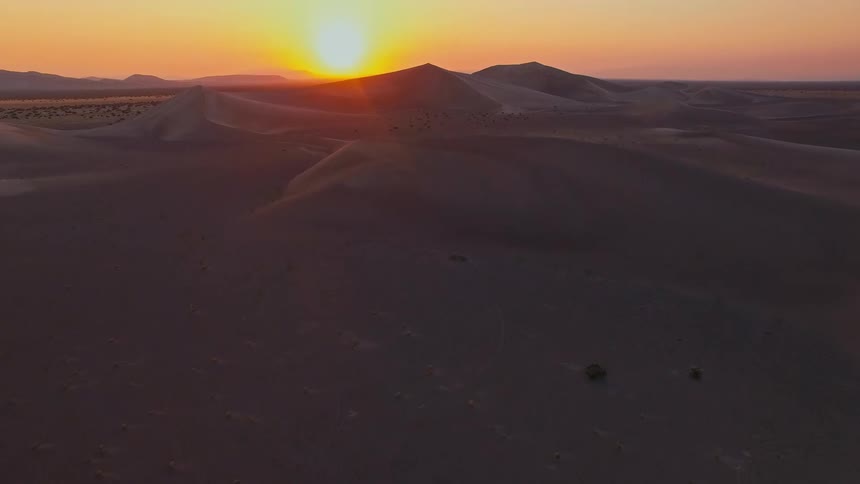 A slow dimly lit shot of a sandy surface at dusk with soft warm light casting gentle shadows across the textured ground