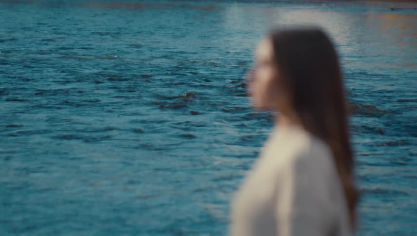 A woman with brown hair stands near a swiftly flowing river