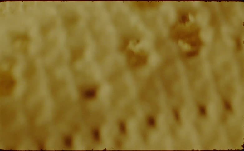 The video shows a closeup shaky texture of what appears to be a light yellow or beige porous material possibly a piece of crocheted or knitted fabric or an abstract interpretation of a perforated surface