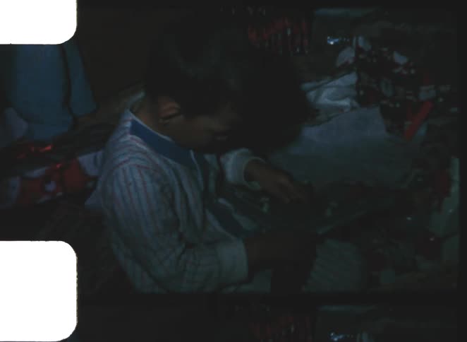 A young child examines a toy rifle indoors among scattered toys in a dim vintage room