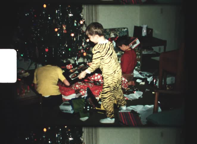 Three young boys open presents near a decorated christmas tree with one standing in tiger striped pajamas
