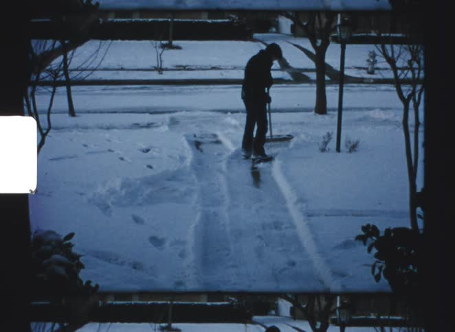 A silhouetted figure shovels snow from a residential driveway