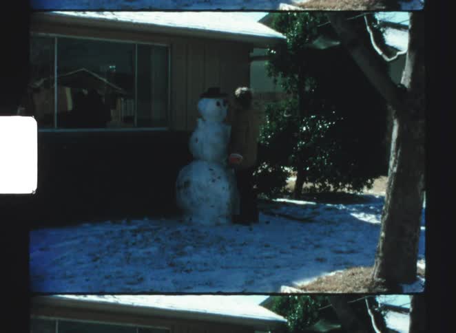 Person adjusting a snowman in front of a house with snow on the ground