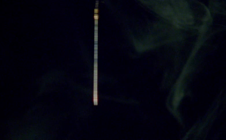 A close view of a stick dropping down in a dark atmosphere surrounded by wisps of smoke