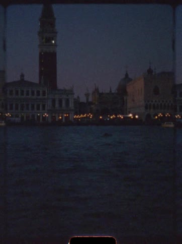 Lit buildings reflect on water in front of st marks campanile on venetian night