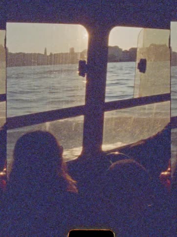 Silhouettes watch sunset through vessel window with view of distant shoreline