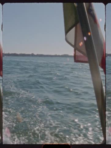 Red and white flag flutters above vessel moving toward the shore