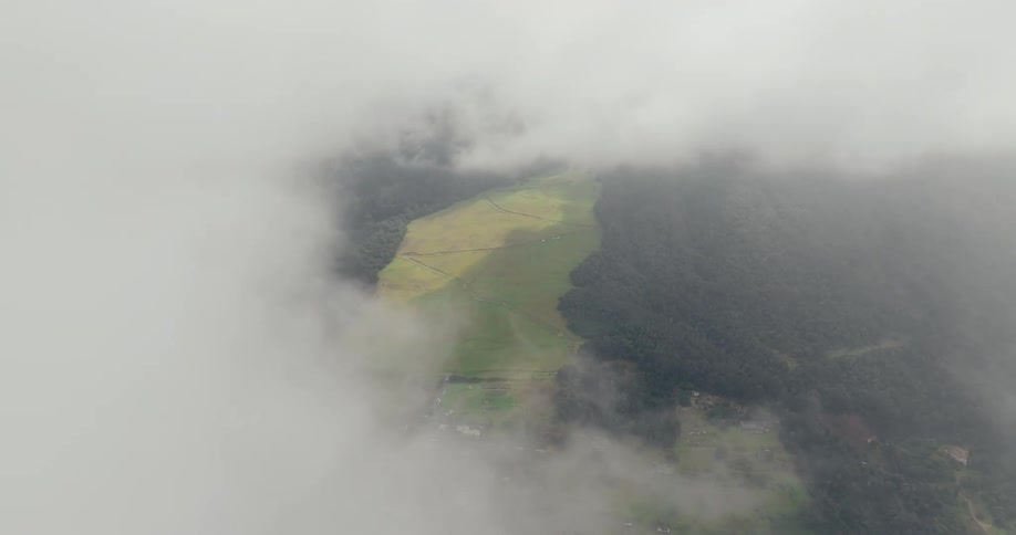 Aerial view of green farmland dividing dense forested hills beneath low clouds and mist