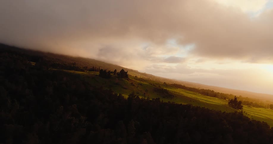 Green hills lit by sunlight beneath low clouds in a rural area
