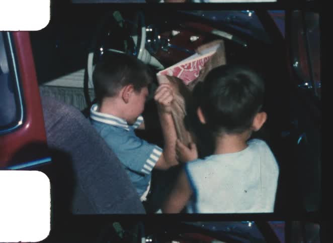 Two children handling a paper bag beside a parked car