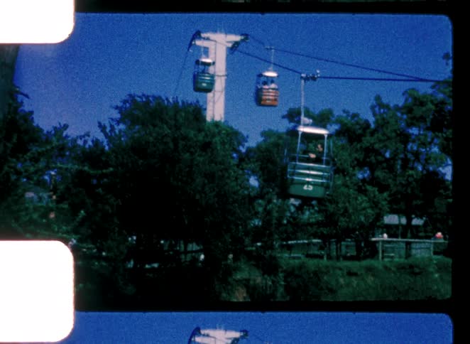 An amusement park bustles with activity at midday with people riding the sky ride high above the ground