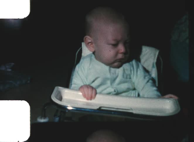 Baby seated in a high chair with a tray in front in an indoor setting