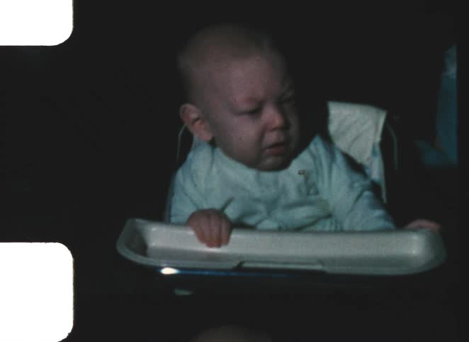 Baby in high chair makes displeased expression