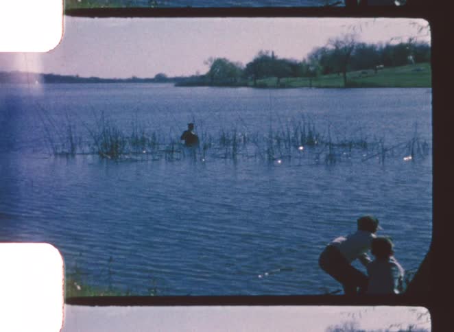 Two kids stand by a lake playfully pulling a small boat toward the shore on a sunny day