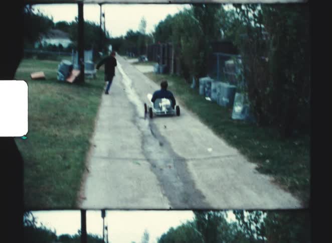 Youth races a friend riding in a cart along the alley between yards on an autumn day