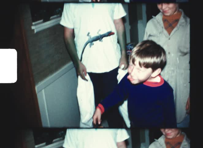 Young boys interact with a man wearing a monster mask and a hat at a nighttime halloween party captured in a vintage 8mm film look