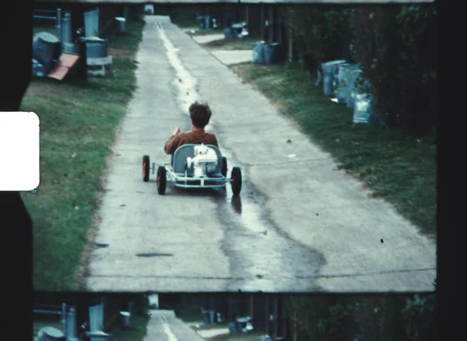 The child is riding a go kart on the sidewalk
