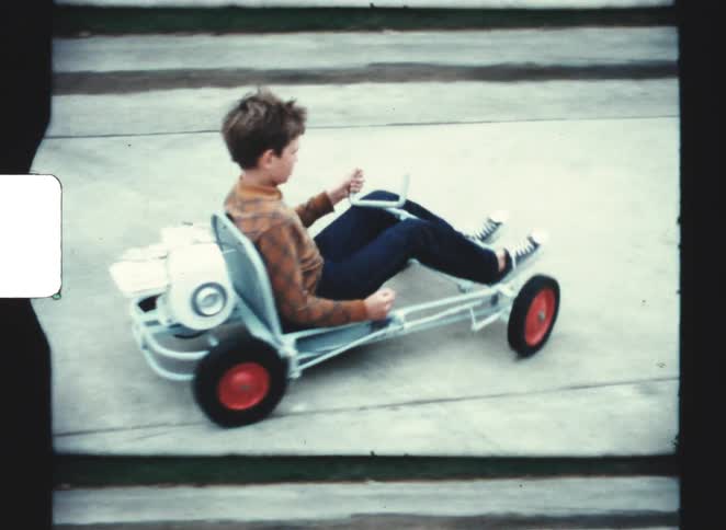A young boy rides a small pedal car along a quiet neighborhood alley