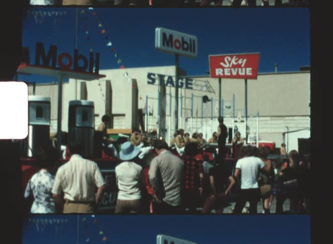 A large crowd gathered at a gas station on a sunny day