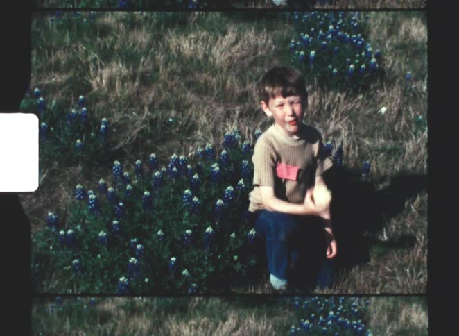 A young boy eats an apple while sitting in a wildflower meadow