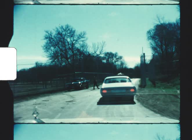 Person walks forward as a car stops near an open gate on a winter day