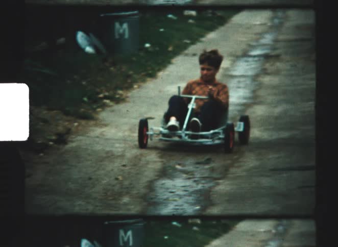 A child riding a homemade gravity racer down an alleyway at midday