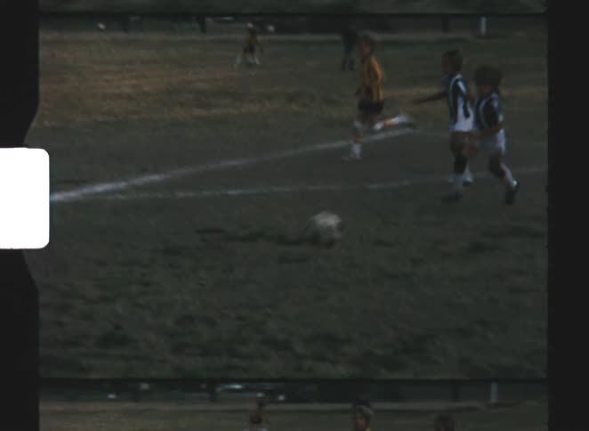 Caught in the motion of a vintage film reel soccer players sprint across a grassy pitch in pursuit of the ball during an energetic match