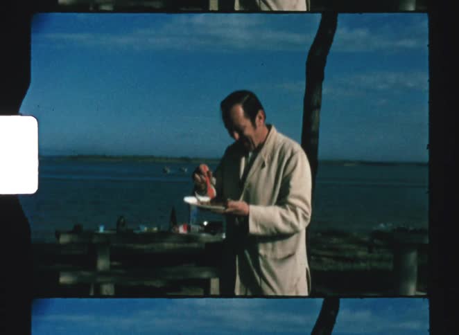The man smiles while eating by the lake