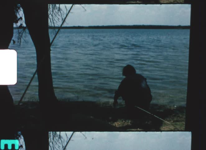 The person is crouching by the shore of the lake