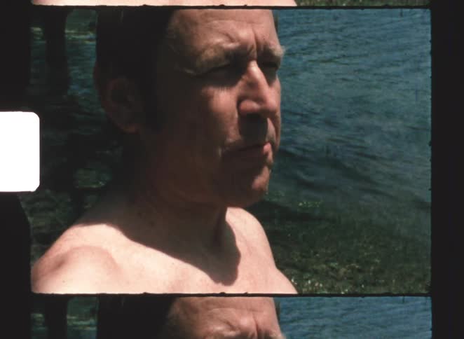 A man eats a banana while sitting at the lakeside on a sunny day