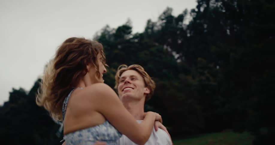 A man and woman run toward each other in a grassy field the woman jumps into his arms and the man lifts and spins her around while they laugh sharing a moment of playful affection outdoors