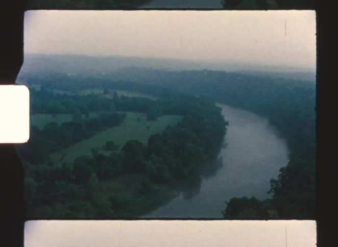 A river running through a rainforest with green vegetation on both sides as it curves to the left at midday