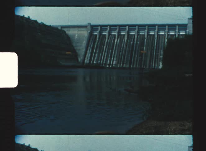 A dam with a large structure and a lowtide river beneath it at midday