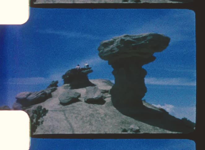Mushroomshaped rock formation stands out in arid landscape with blue sky and visitors in background