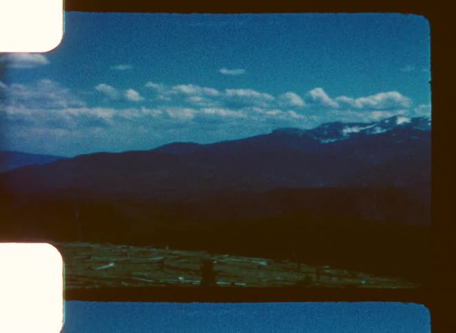 A grassland on a hill with a snowcovered mountain range in the background at midday